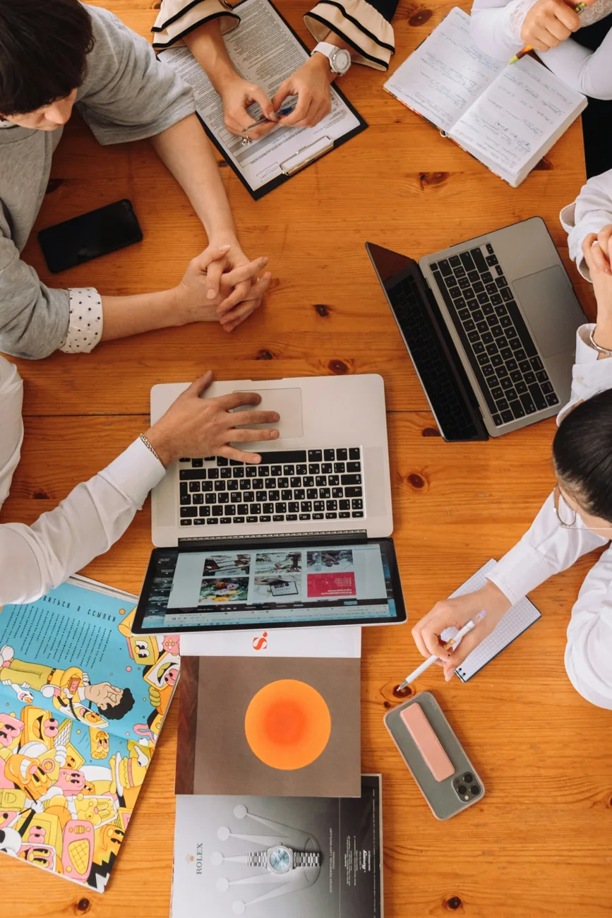 Illustrative photograph of adults collaborating around laptops and notebooks